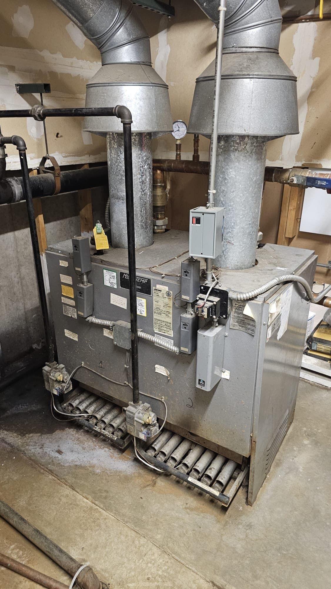 Commercial gas boiler with two galvanized flue pipes in a utility room