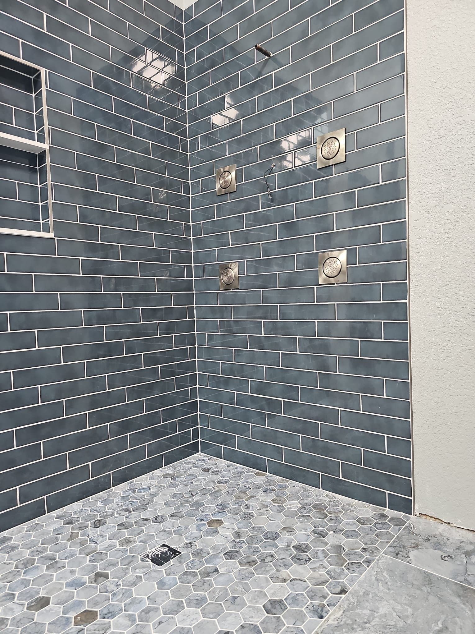 Finished shower by Lukenbuilt with blue tile walls, chrome body spray jets and a hex tile floor